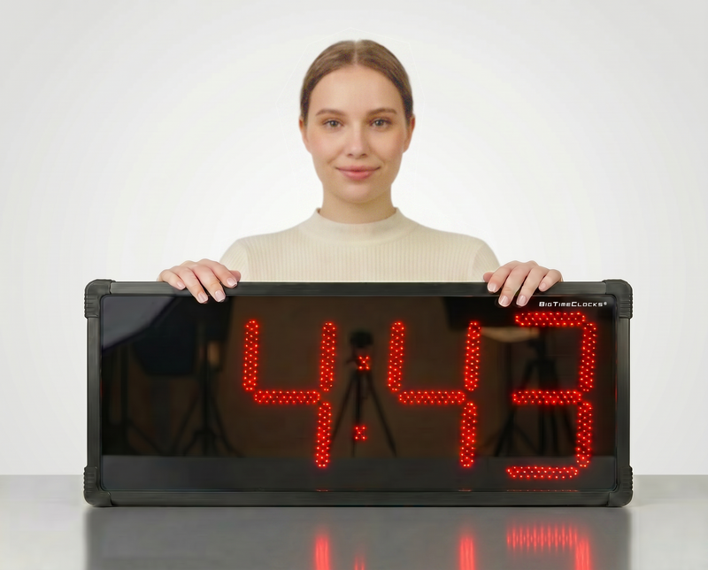 Woman holding a BigTimeclocks digital clock displaying 4:43 on a white background