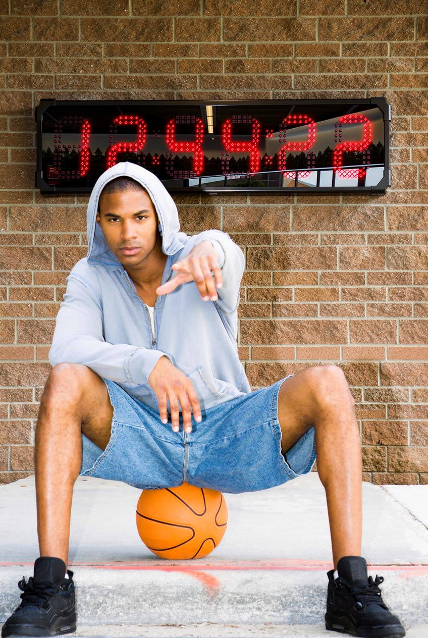 Person sitting on a basketball with a BigTimeClocks digital waterproof clock displaying time in the background