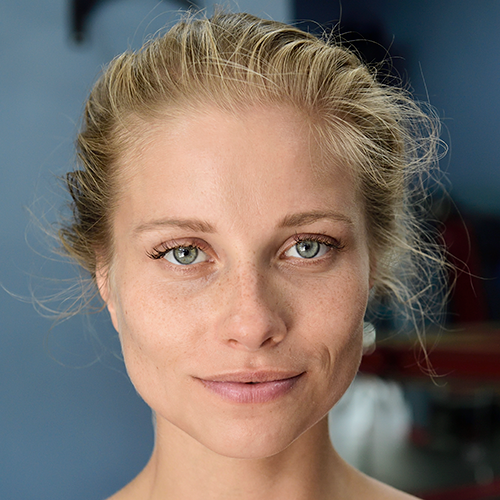 Close-up of a person with blonde hair and blue eyes against a blurred background